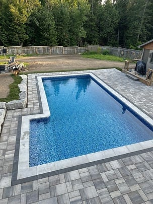 Rectangular backyard swimming pool with blue water surrounded by gray paver patio and wooden fence